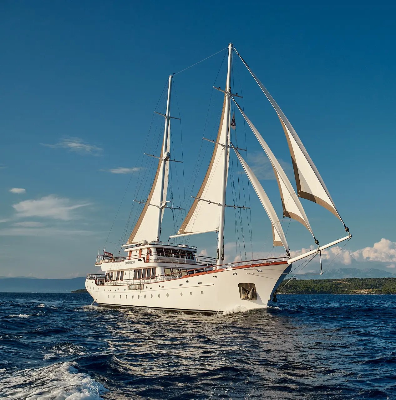 Corsario – front view with full sails, cruising through clear blue waters under bright skies