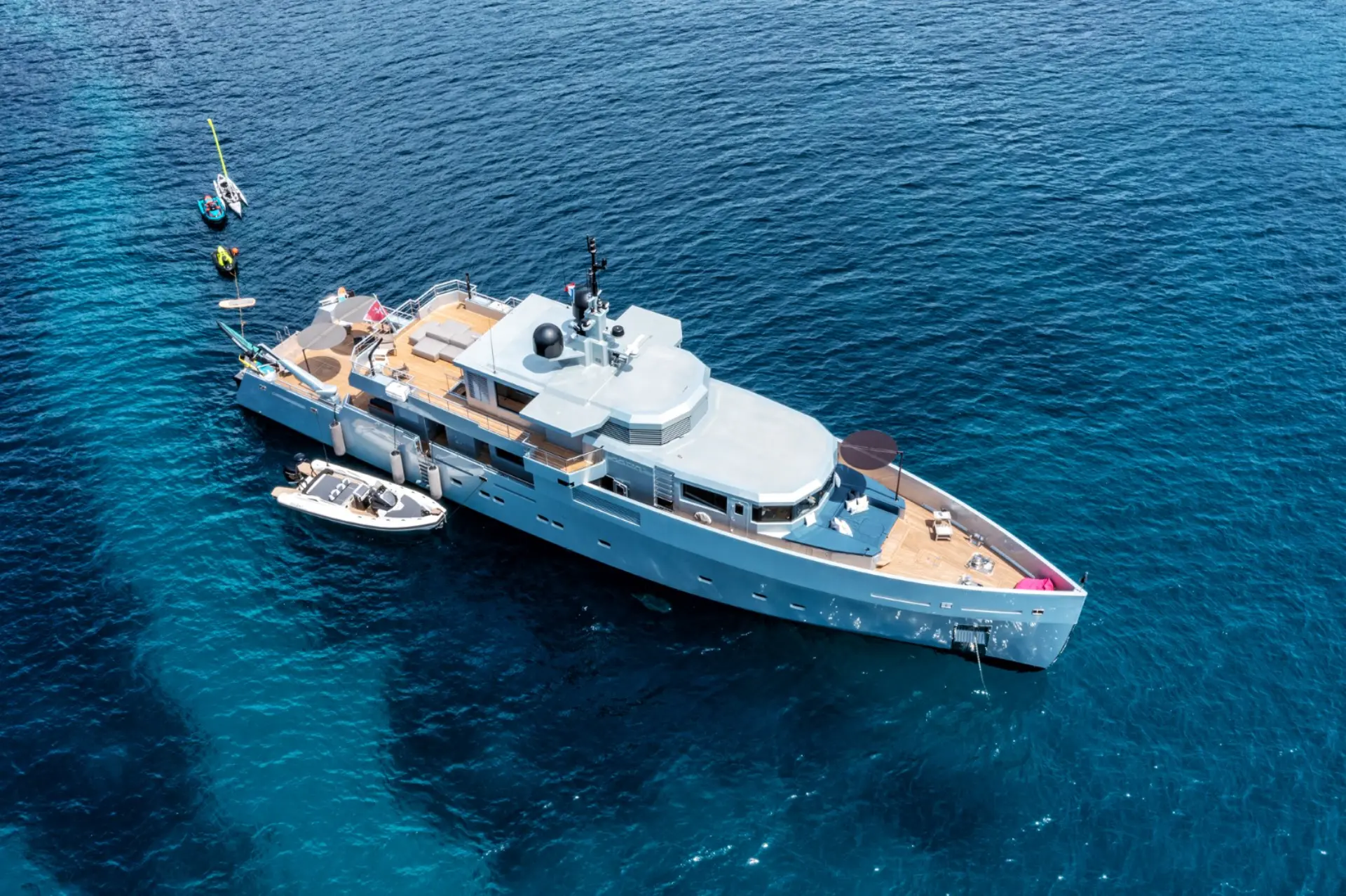 Luxury motor yacht Caladan – aerial view with tender and water toys lined up at stern, surrounded by vibrant blue sea.