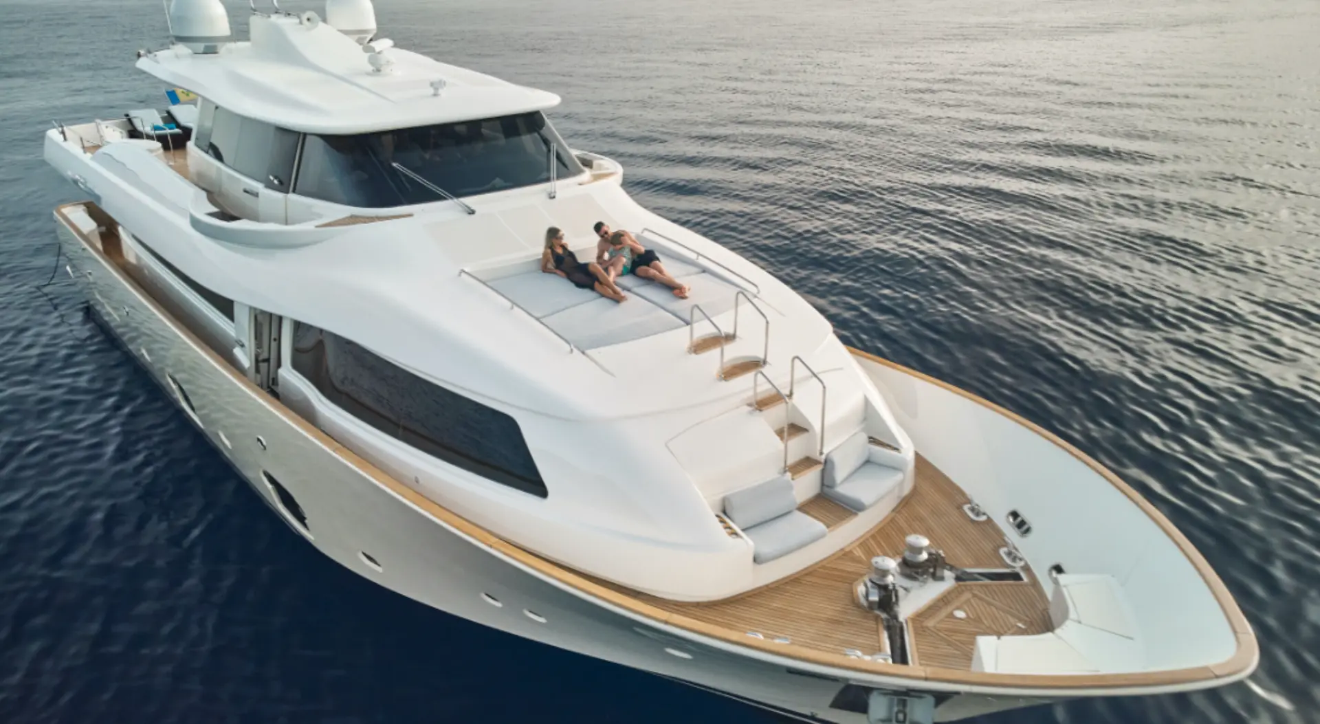 Luxury motor yacht Navetta 26 – aerial close view, foredeck with two guests relaxing and sunbathing in scenic Adriatic bay.