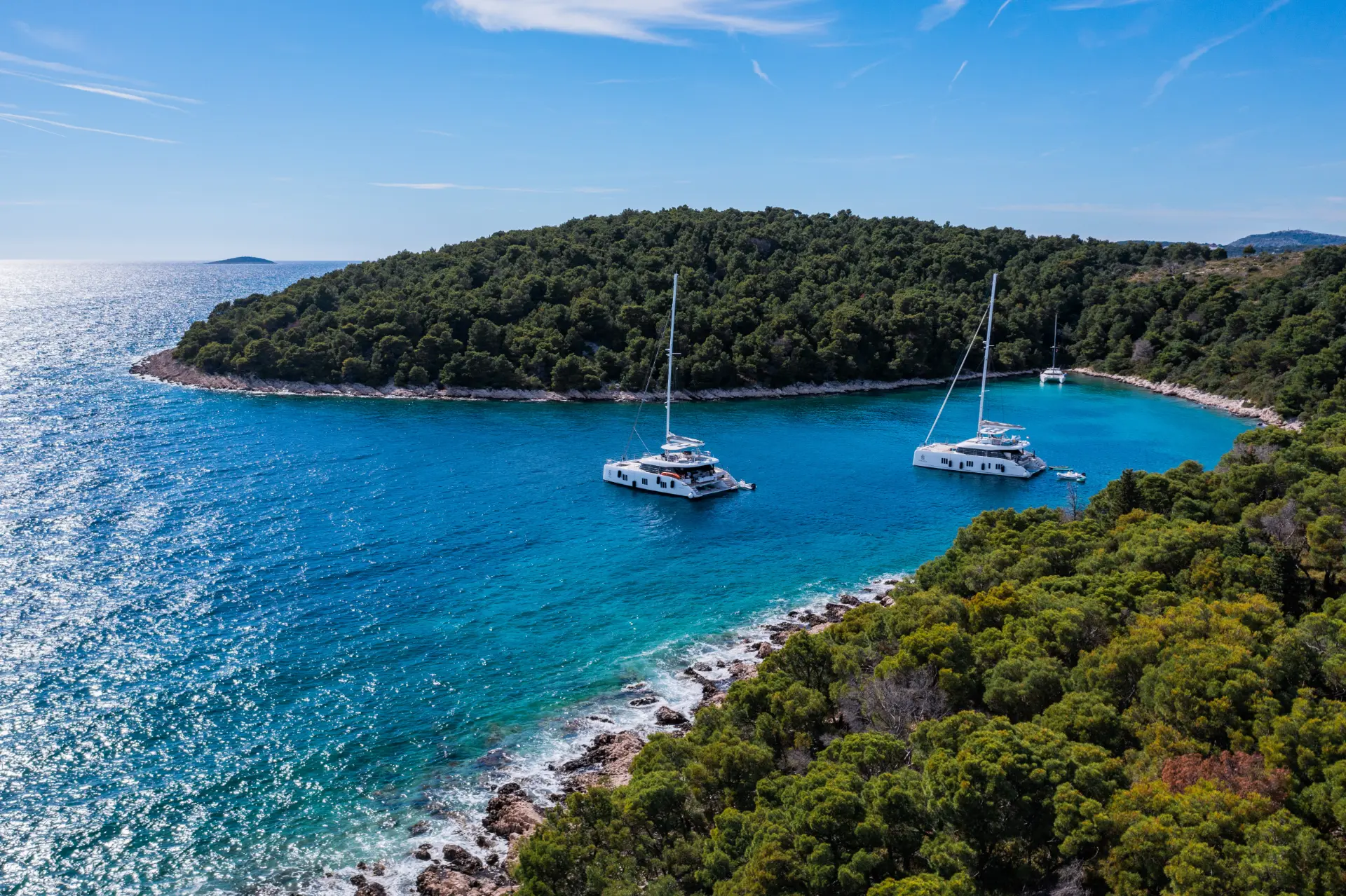 Sunreef 60 in the nice bay with greenery around, basking in the afternoon sun near the coast.