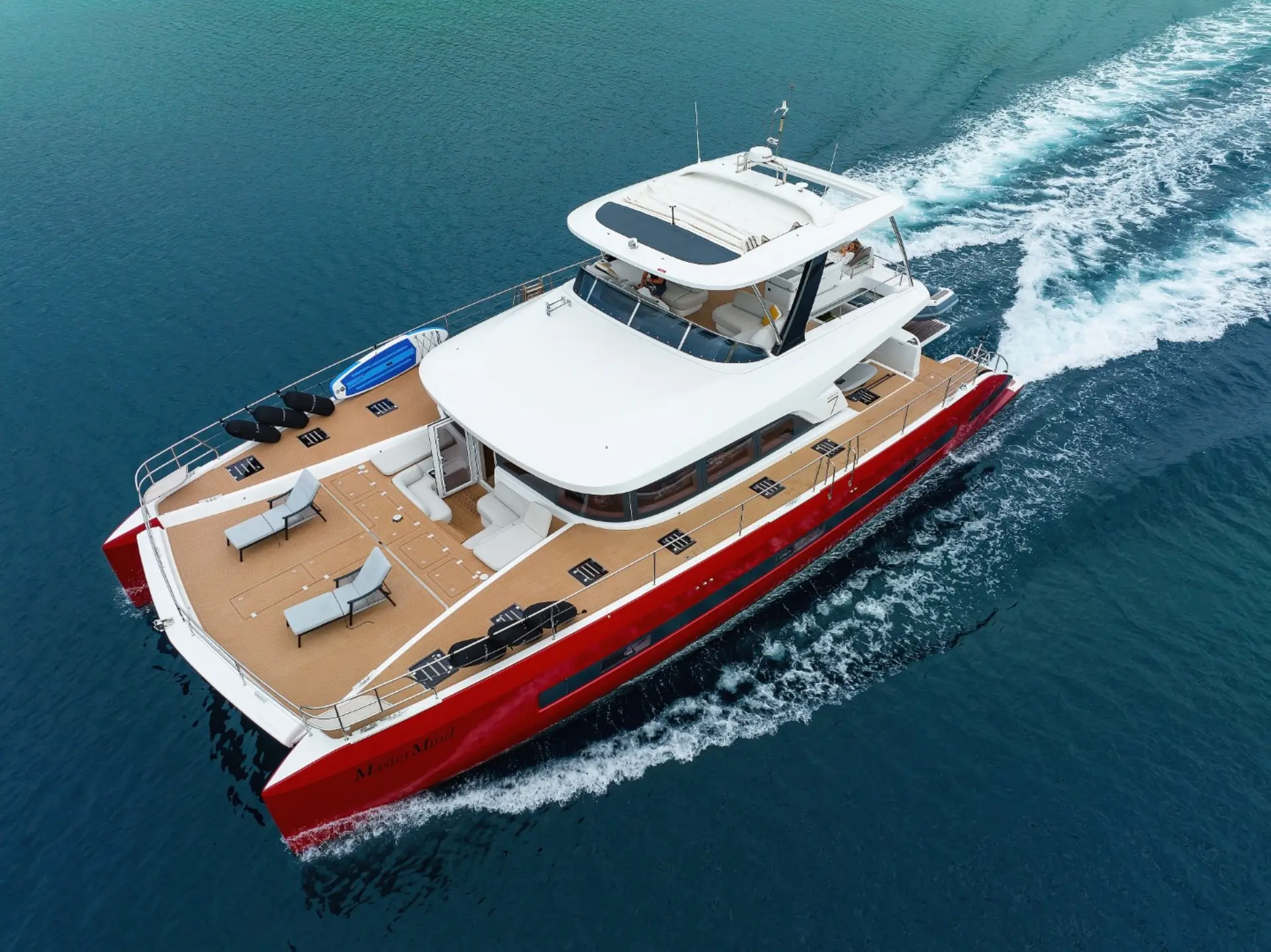 Luxury catamaran Lagoon Sixty 7 – overhead front angle gliding across bright blue waters, showcasing her bold red hull.