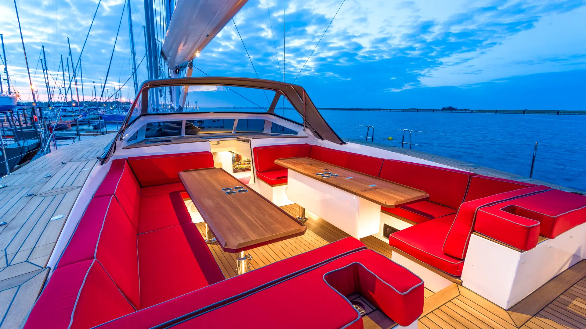 Bellkara - aft cockpit view with two tables, red cushions, and masts of other yachts visible in the background.