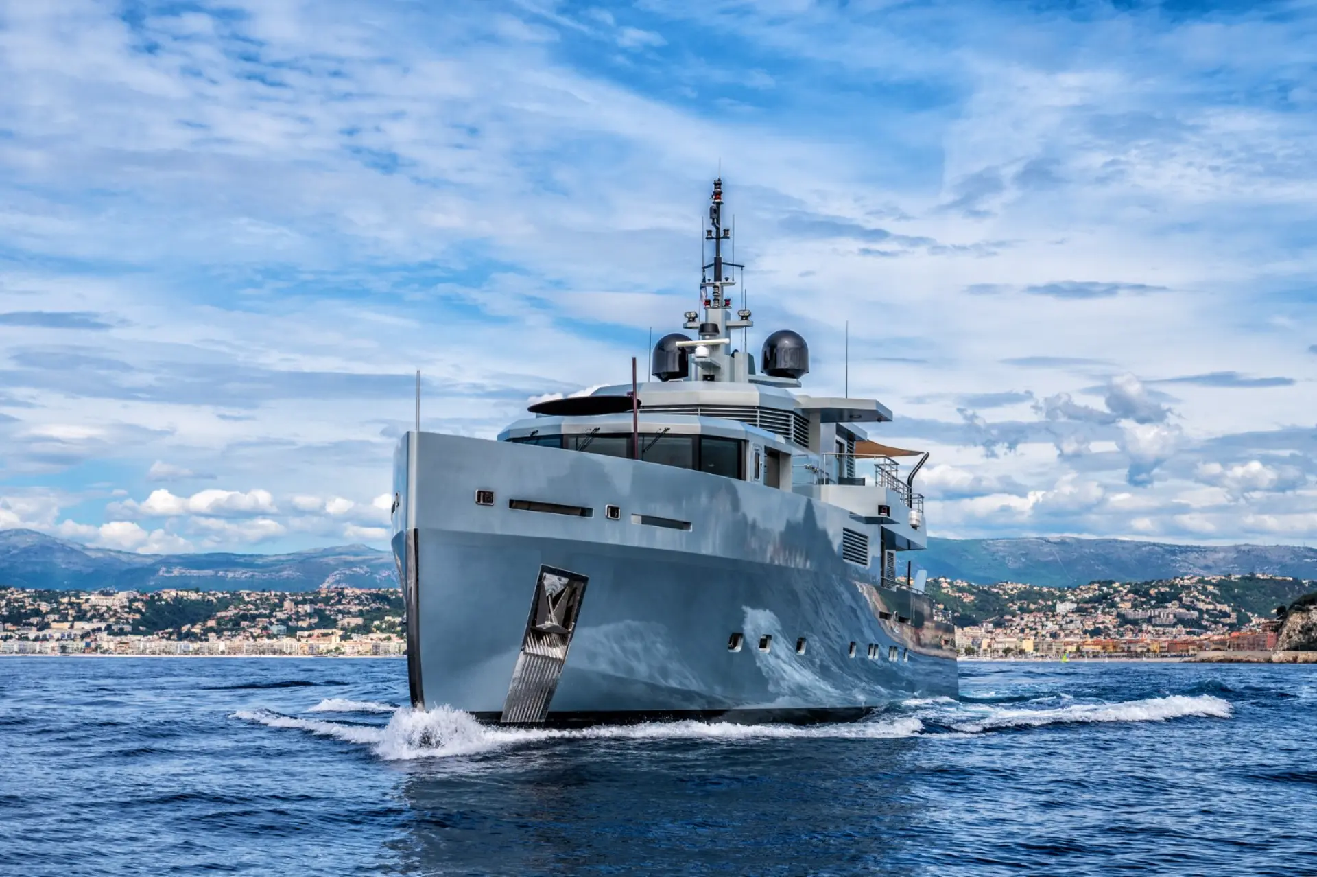 Caladan – yacht cruising forward, city silhouette visible behind on the horizon.