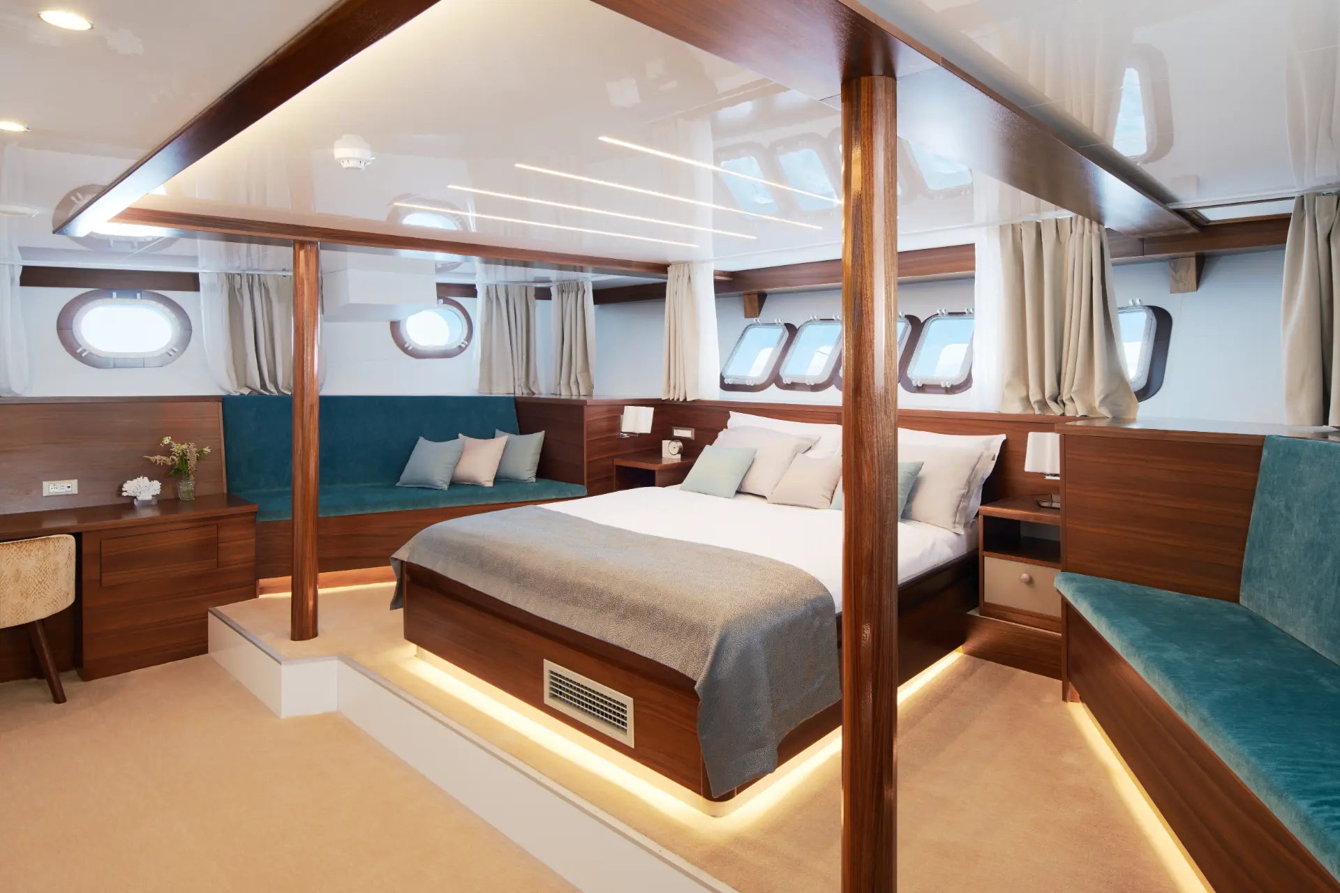 Corsario master bedroom featuring bed, blue cushioned seats flanking both sides, and a desk in view.