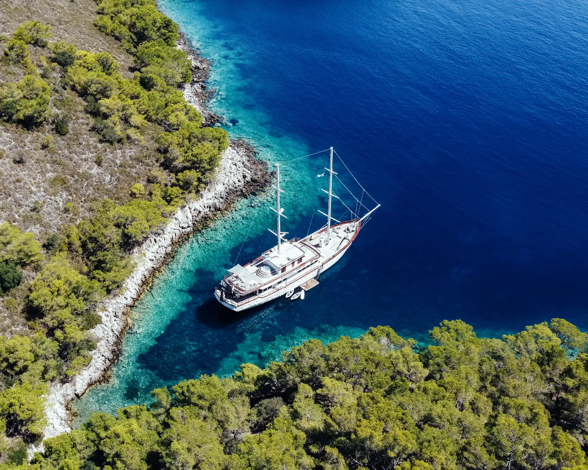 Luxury sailing yacht Corsario - aerial top view, yacht anchored in turquoise bay, stunning Croatian coastline in background