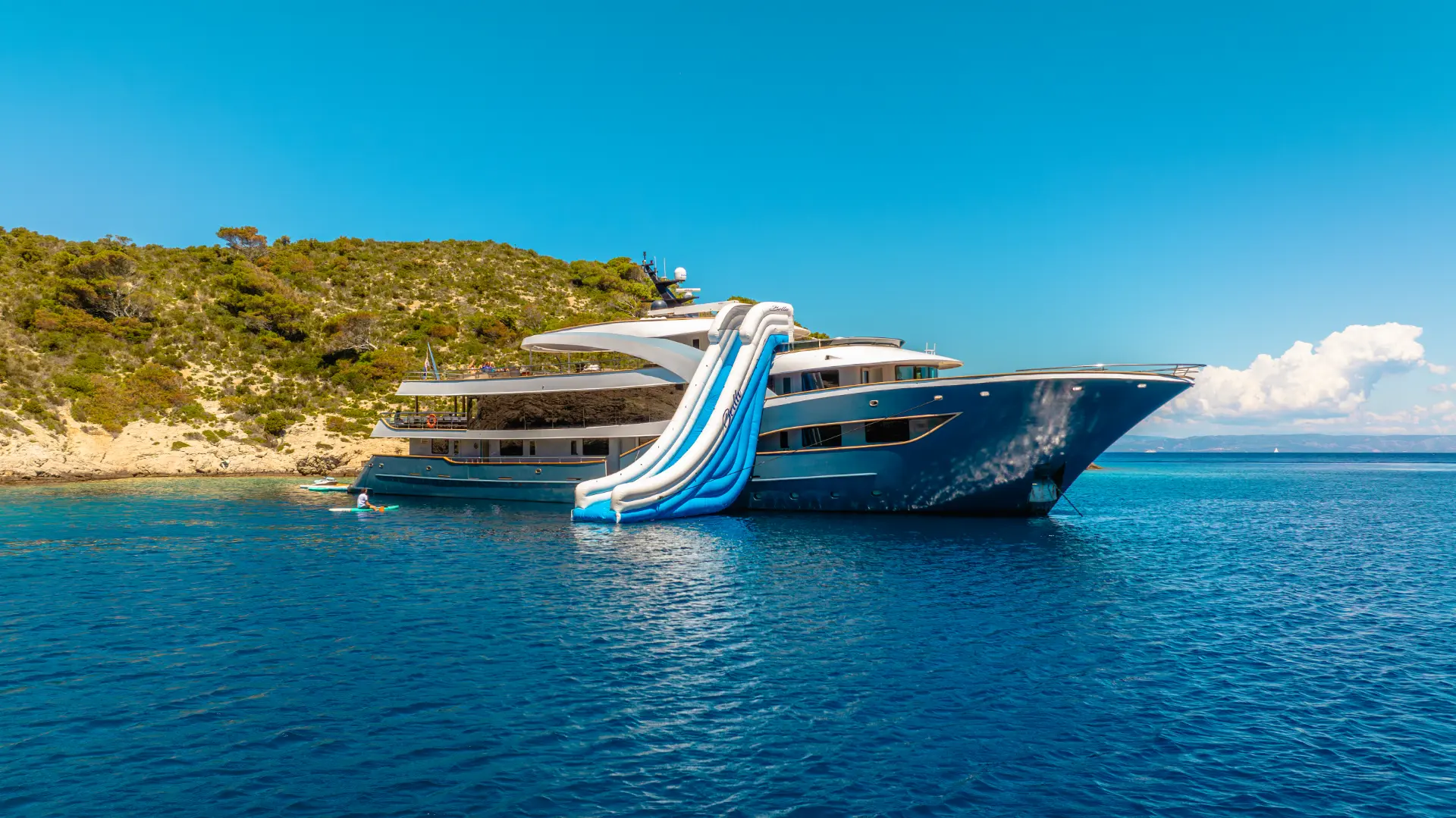 Bella – peaceful bay anchorage, side view with waterslide and vibrant greenery all around.
