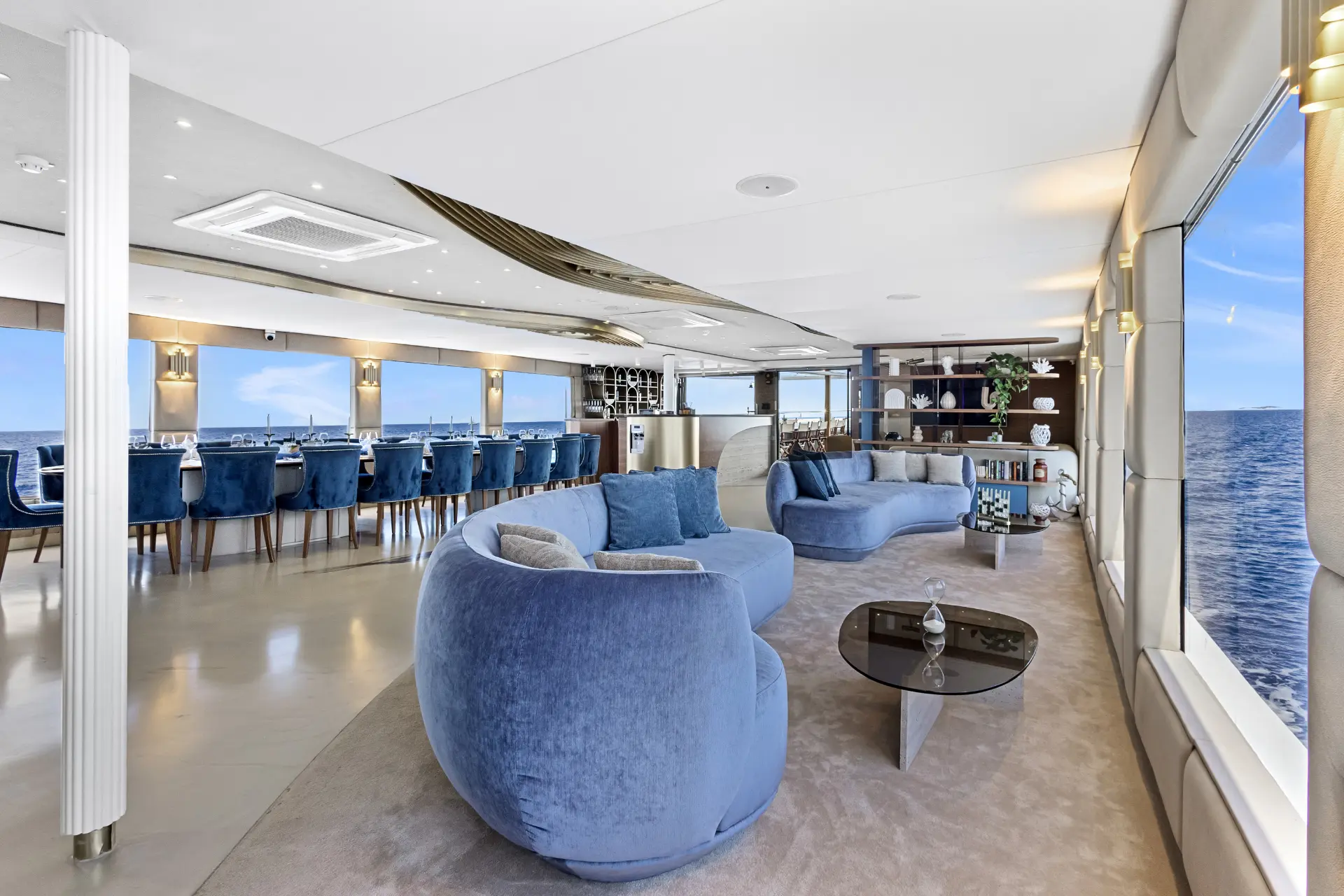 Bella – Elegant salon looking towards entrance, dining tables left, soft seating right, encased by wide floor-to-ceiling windows.