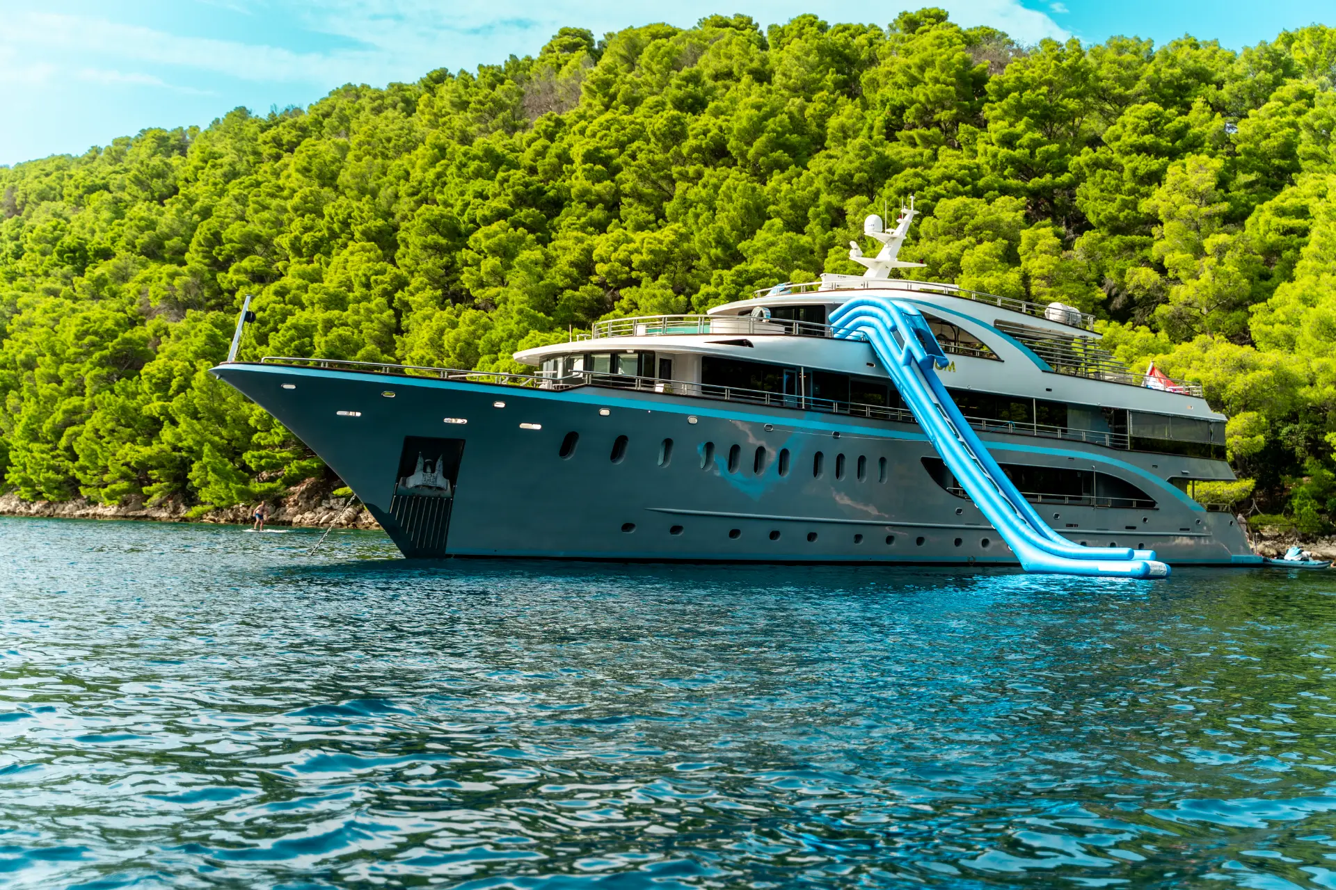 Freedom – close-up side angle, yacht with waterslide in green-fringed turquoise bay