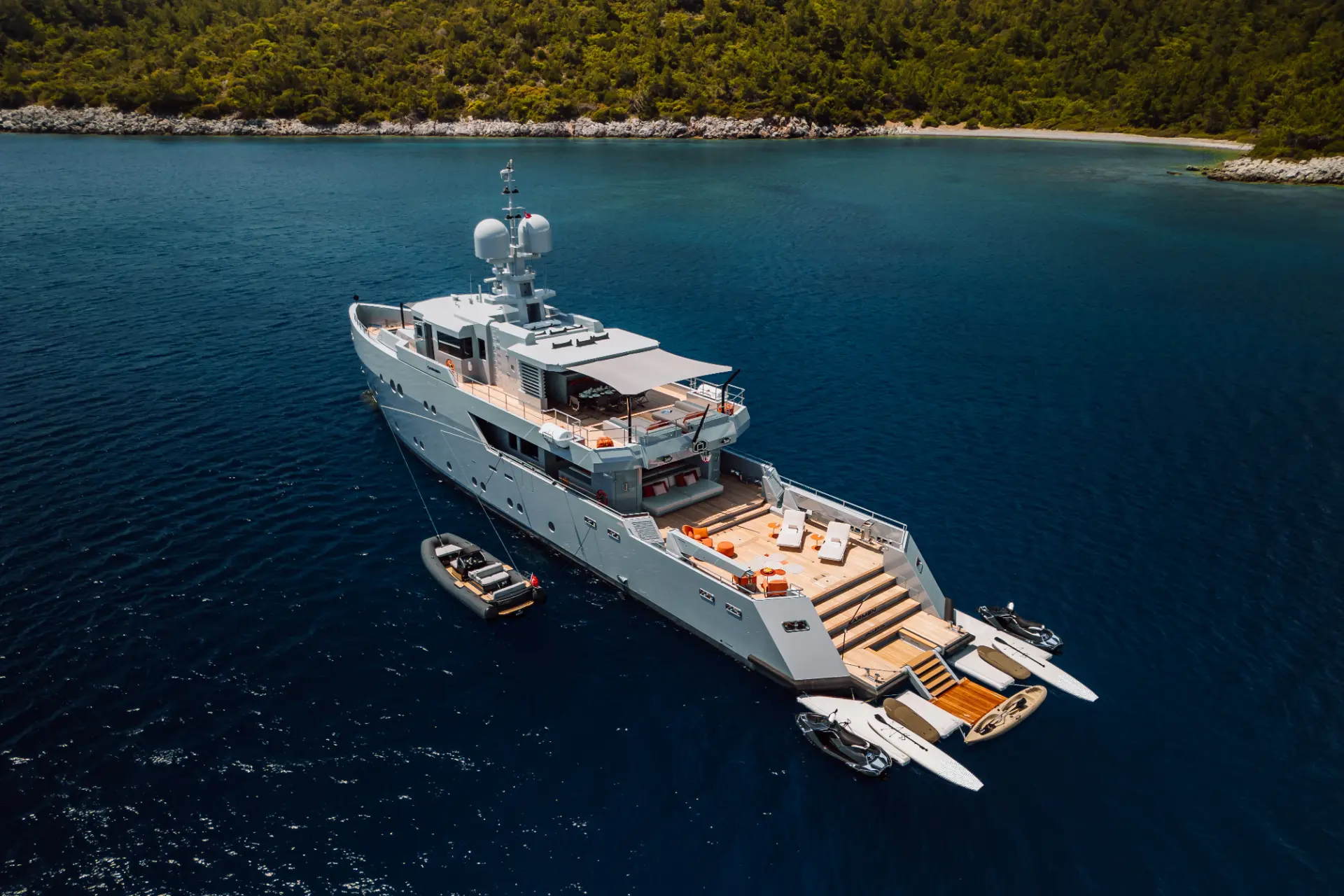 Luxury motor yacht Carmen – resting in a tranquil turquoise bay, green shore in the distance, aft view perspective.