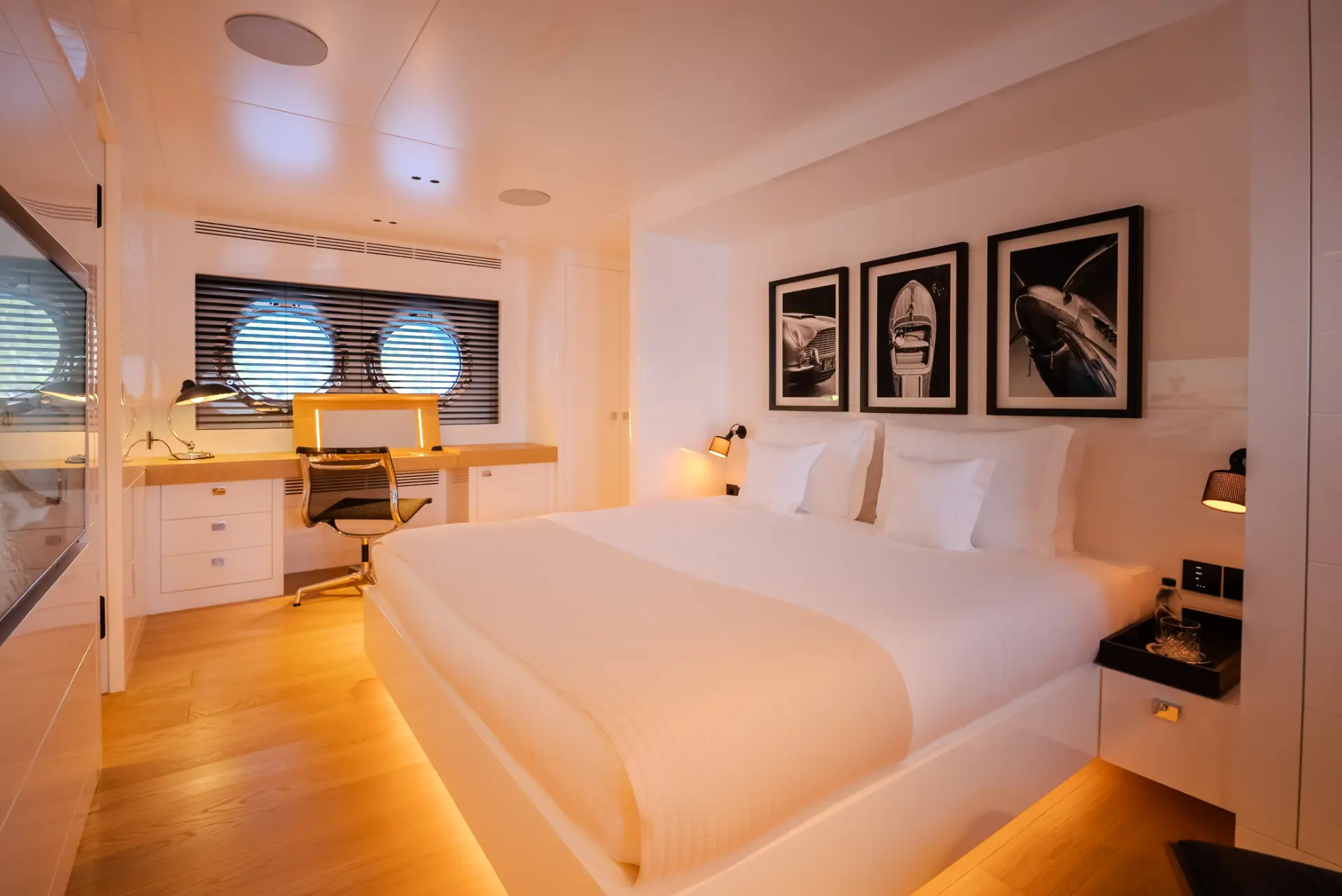 Full-beam master suite on Carmen featuring double bed, artwork, desk with chair, and two round windows.
