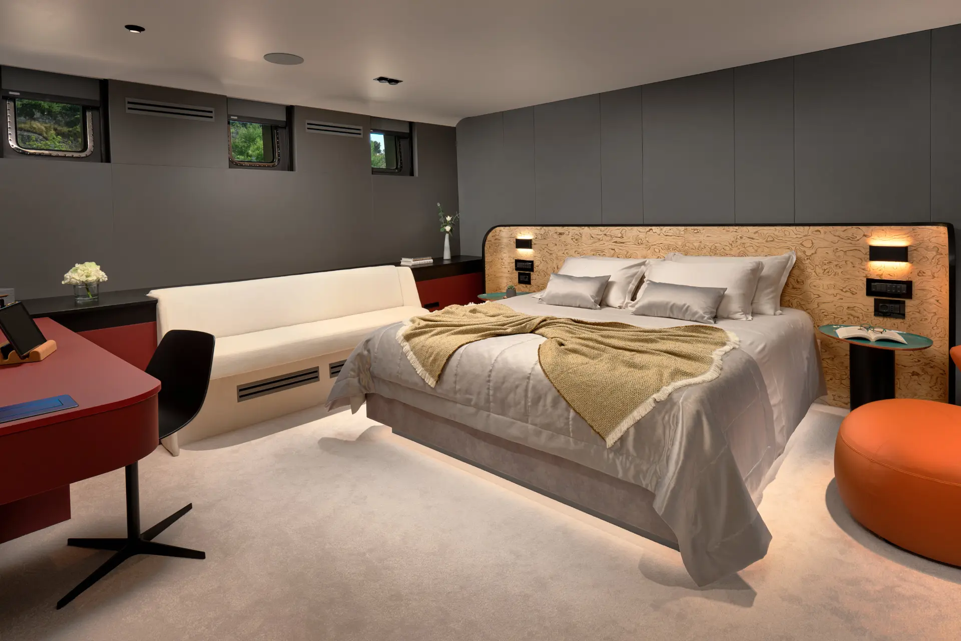 Anetta master cabin featuring a cozy bed, modern desk, sofa, and porthole windows.