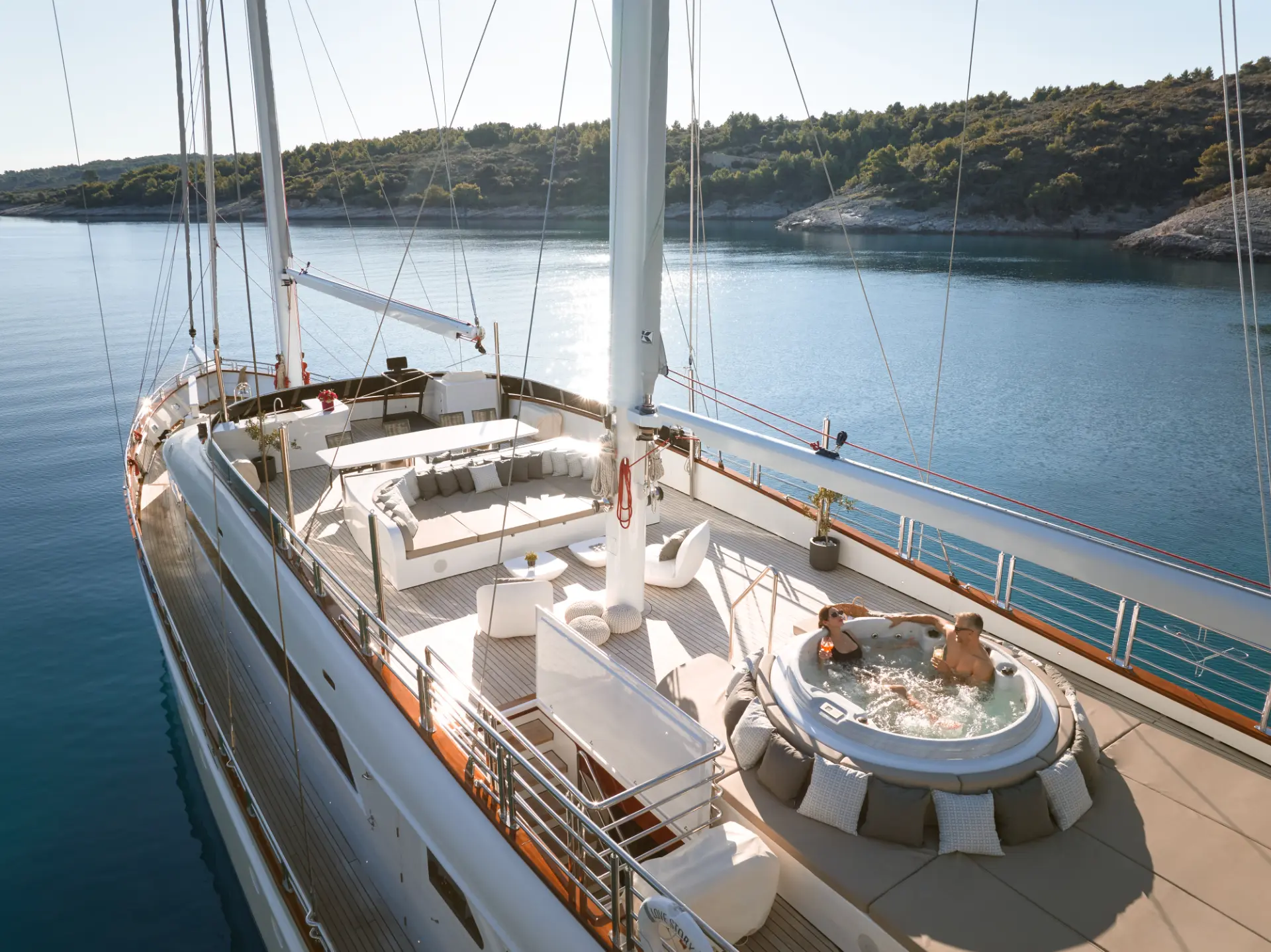 Love Story yacht, aerial daytime close-up of sundeck showing couple enjoying cocktails in jacuzzi.