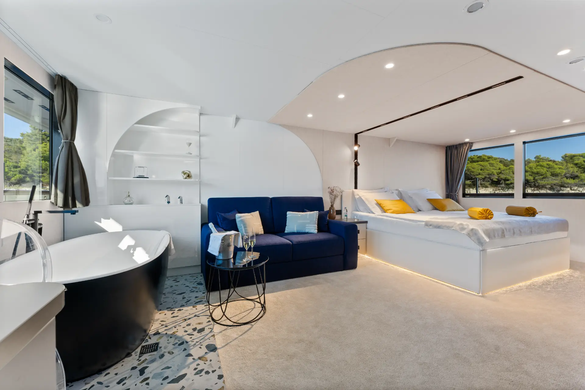 Alfa Mario – bright master cabin with bathtub, comfy seating, small table, bed, and greenery view