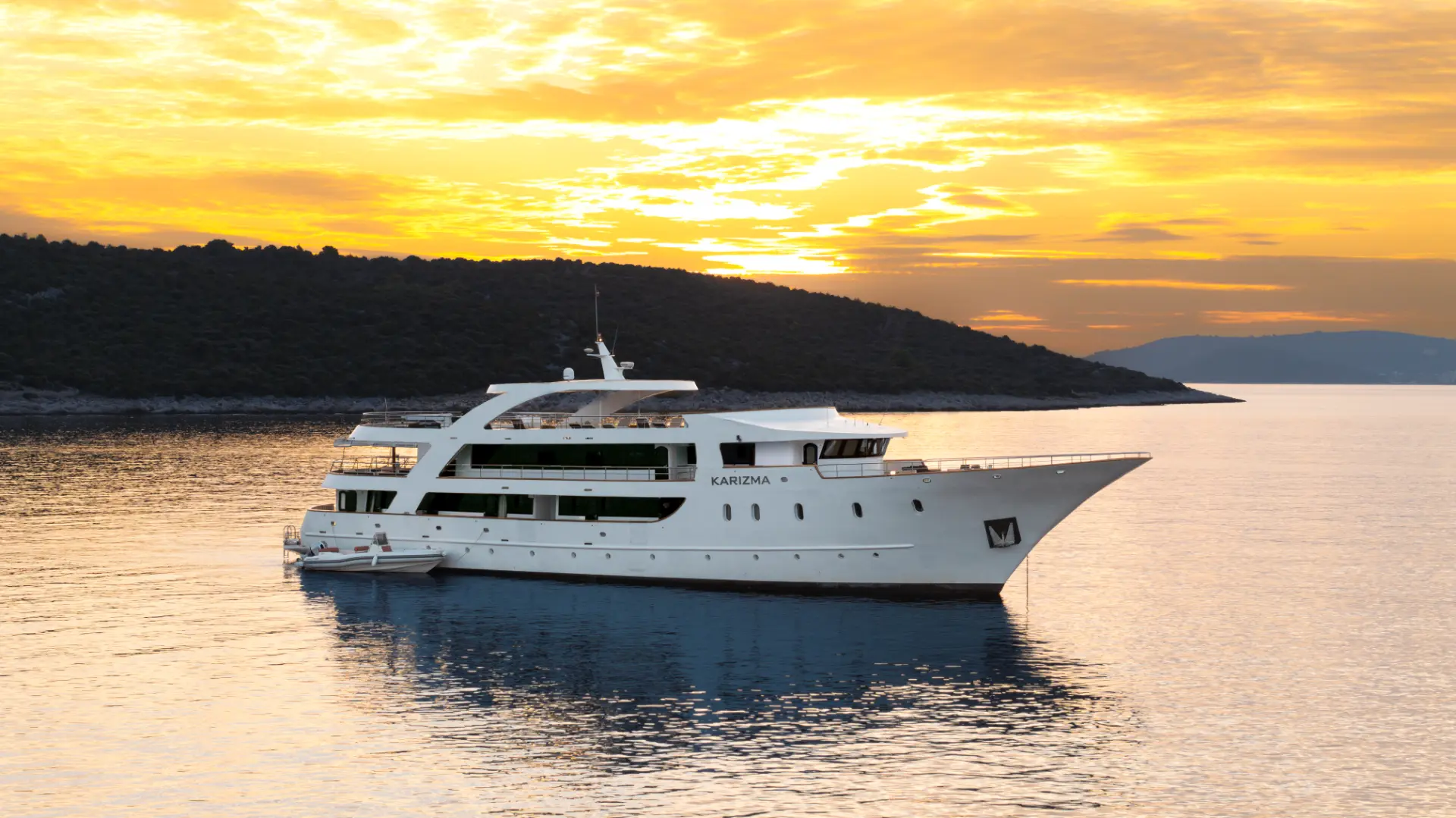Luxury mini cruiser Karizma - side view at anchor, sunset glow and lush coastal backdrop