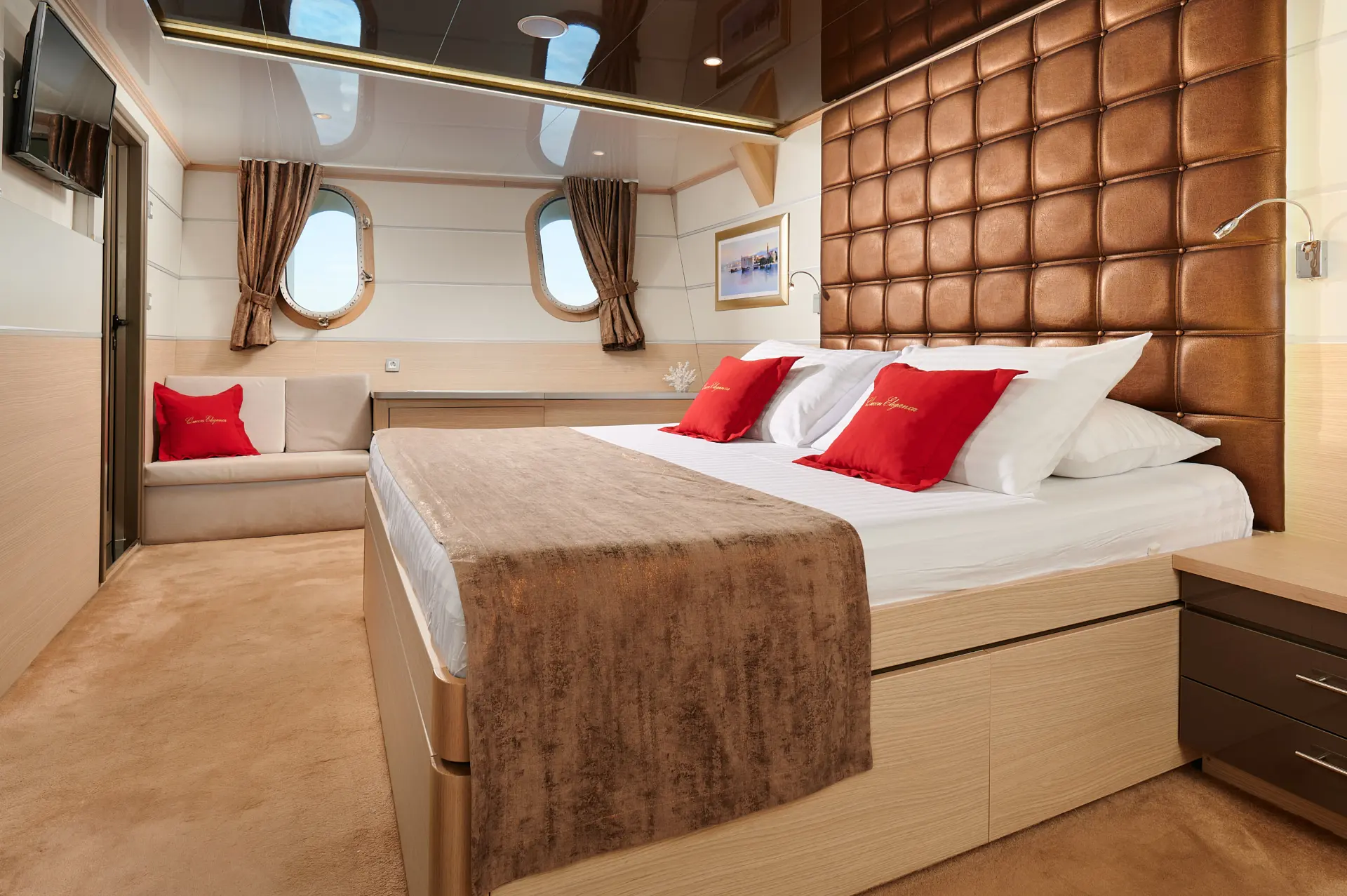 Queen Eleganza – side view of double bed, two small windows, comfortable seating, TV, red decorative touches
