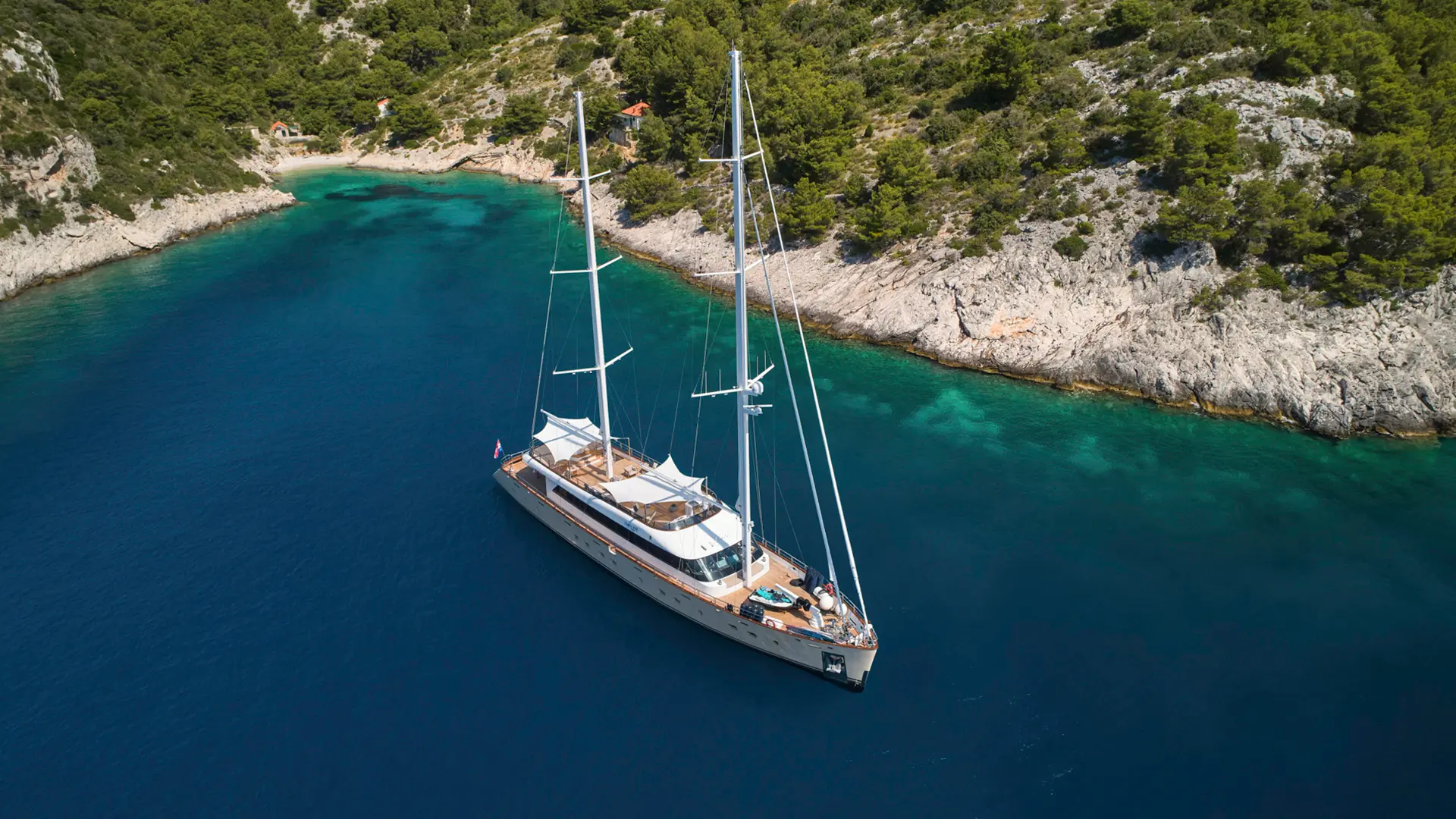 Luxury sailing yacht MarAllure – bow-forward aerial shot in a crystal-clear turquoise bay, surrounded by natural beauty