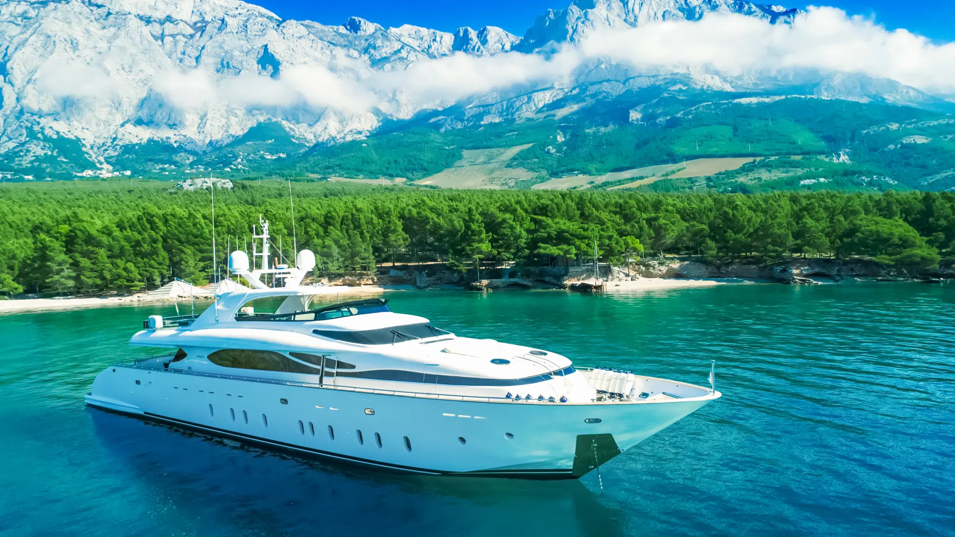 Luxury Motor Yacht Cynthia - anchored, side profile with serene green coastline in the background