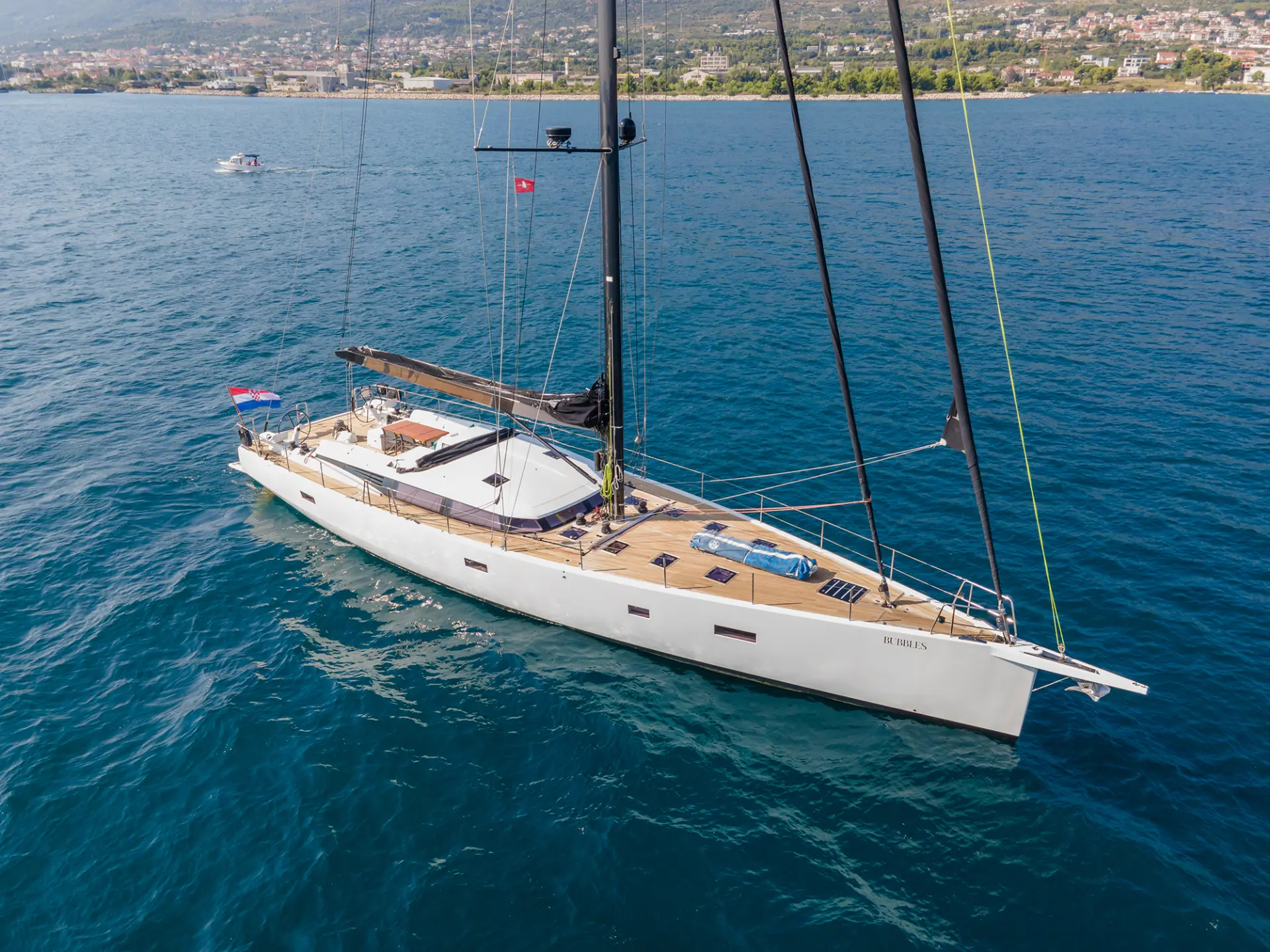 Luxury sailing yacht CNB 76 – yacht at rest, portside view without sails, scenic mountain backdrop.