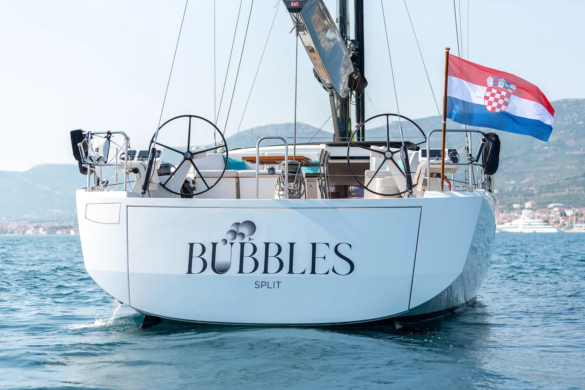 Luxury sailing yacht CNB 76 – Croatian flag at stern, aft view of anchored yacht, surrounded by Adriatic scenery.