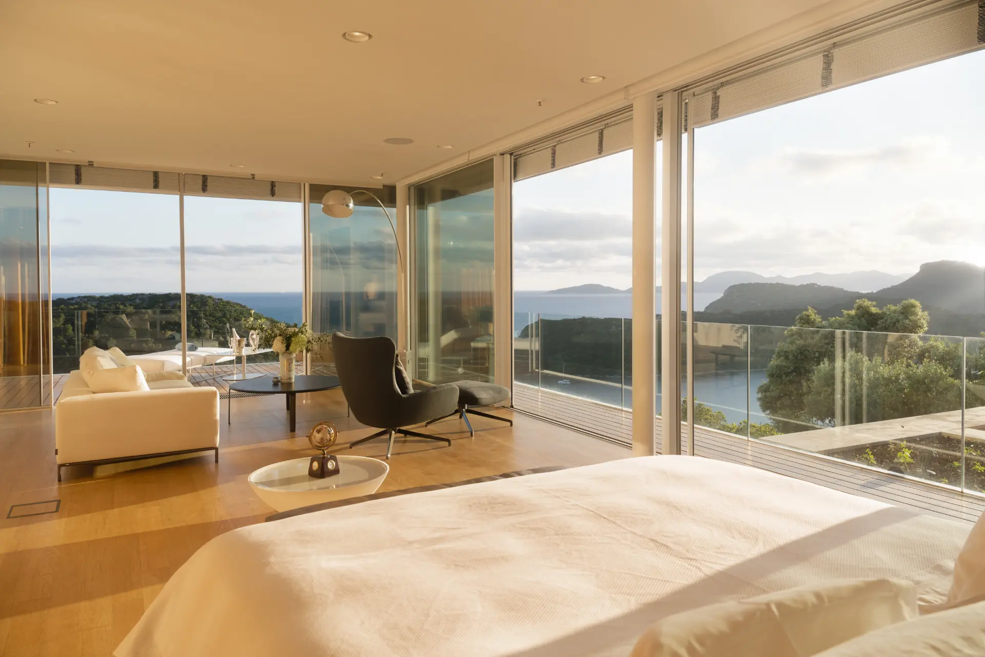 Luxury Estate – double bedroom featuring glass walls, cozy seating, table, and terrace with sunbeds overlooking sea