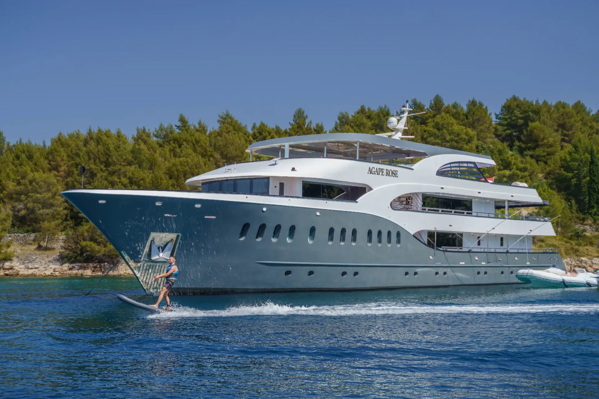 Luxury mini cruiser Agape Rose - Anchored, port side visible; man riding eFoil in foreground, gray tones.