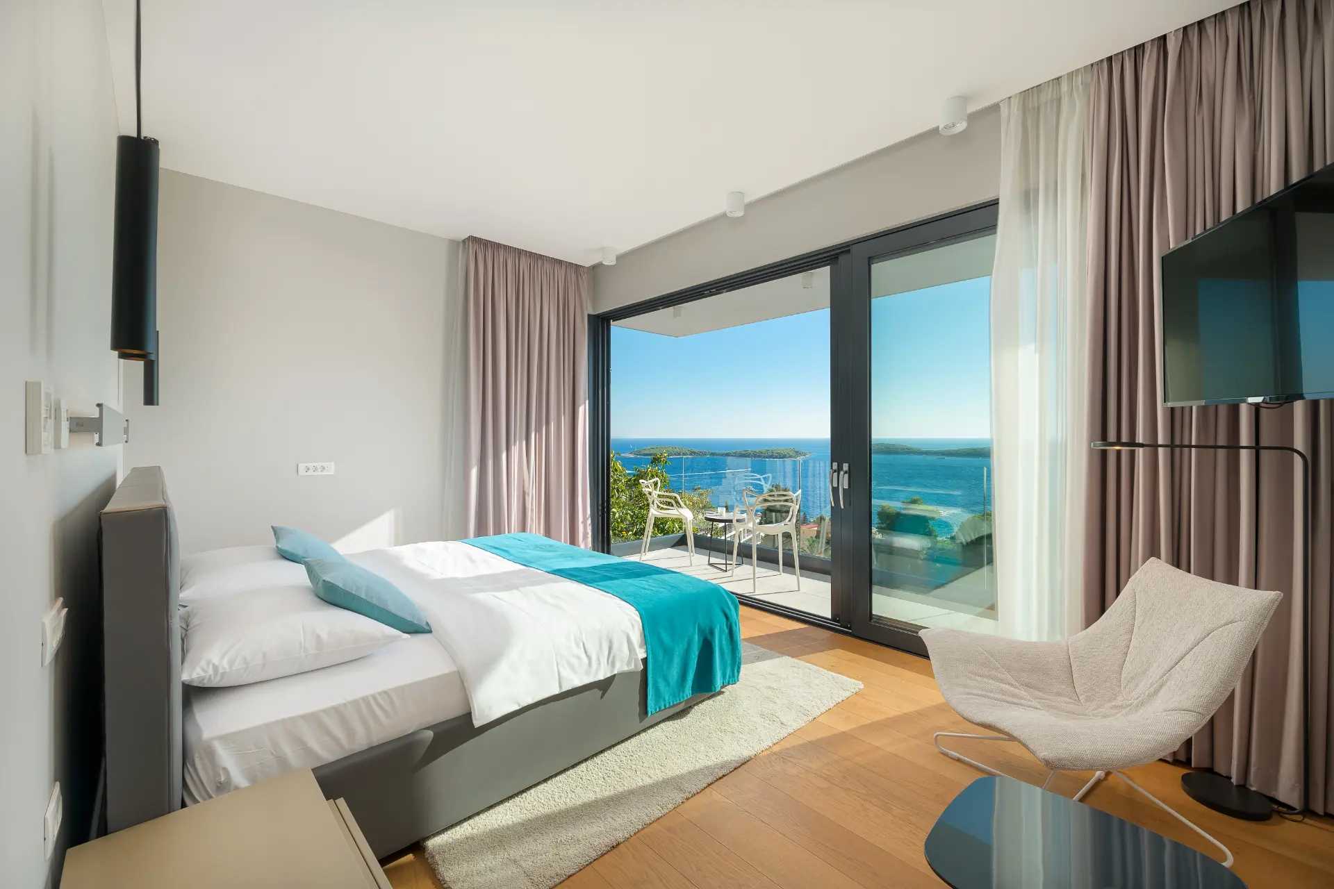Bedroom with large glass door, balcony with small table and 2 chairs, sea view, blue-white bed and comfortable armchair