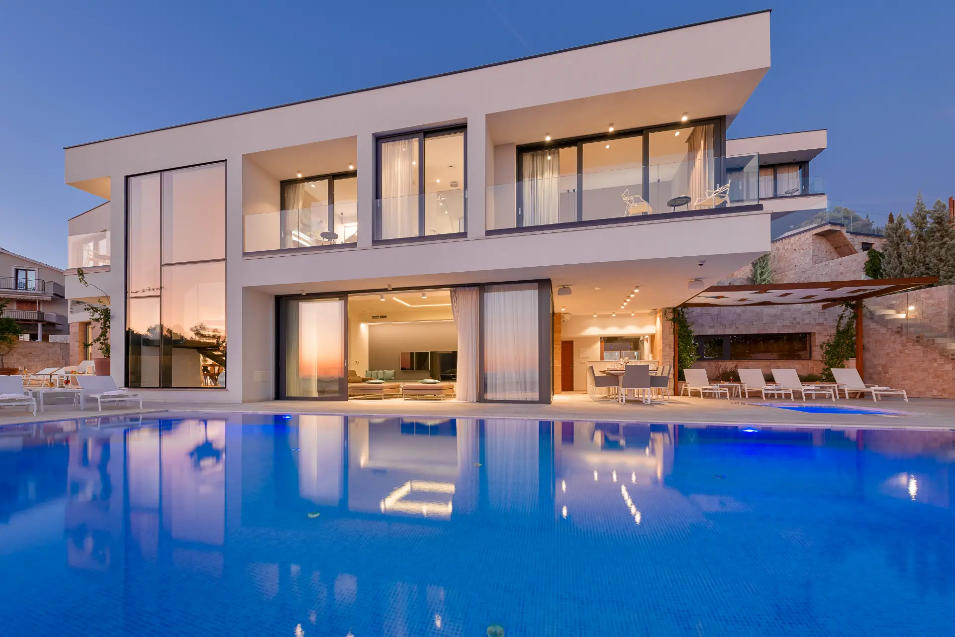 Illuminated at dusk, close view of pool and front villa facade with warm lighting highlighting modern architecture and outdoor space