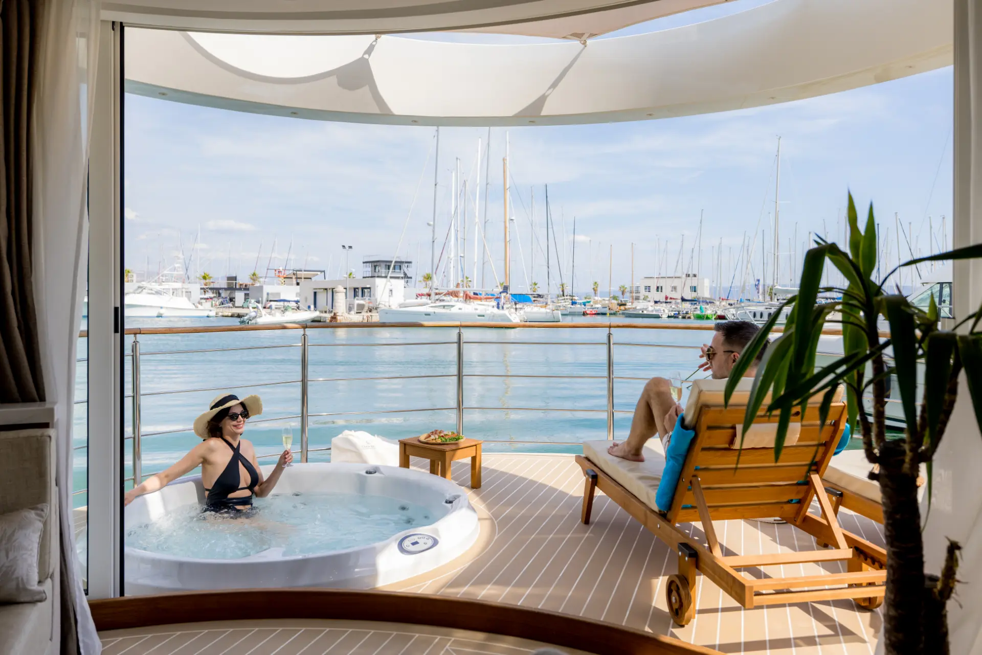 Bow deck of Floating House Amor featuring jacuzzi with woman relaxing, man on deck lounger, Split marina and yachts behind