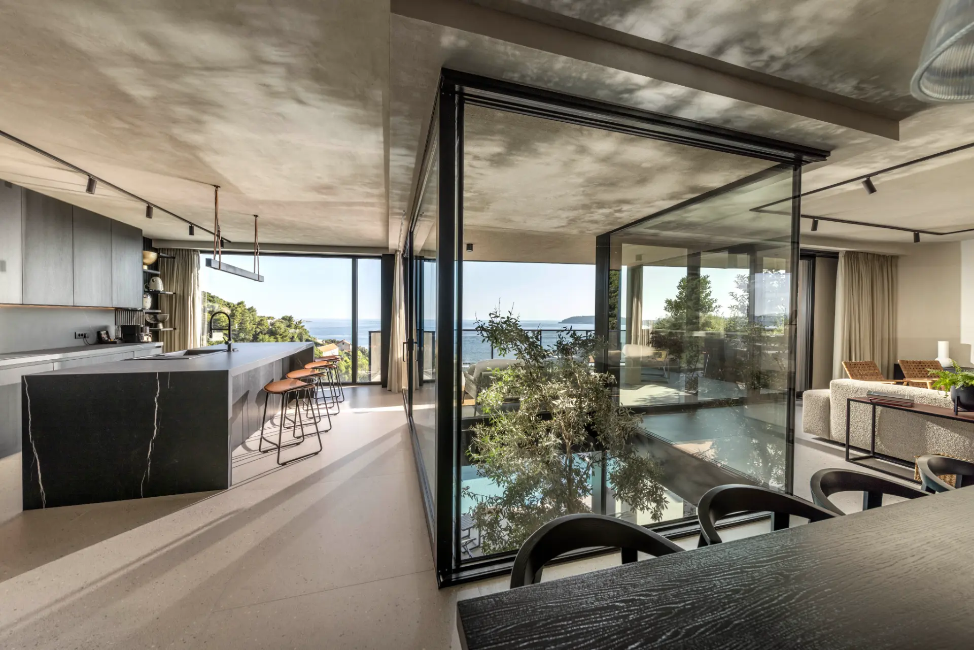 Villa Aurea - contemporary open-plan interior with dining table front, kitchen on left, lounge on right and glass wall with plants