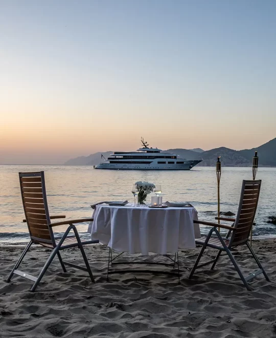 A tranquil sunset over the sea with Black Swan in view from a sandy beach, bathed in warm hues and gentle evening light.
