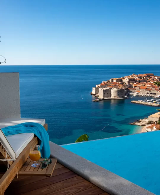 Dubrovnik Villas: Outdoor lounge with infinity pool, sunbed, and cocktail, offering a clear view of Old Town Dubrovnik.