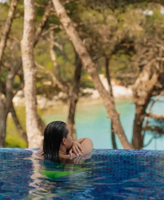At Villa Heidi, a woman enjoys the poolside, surrounded by greenery and overlooking the sea.